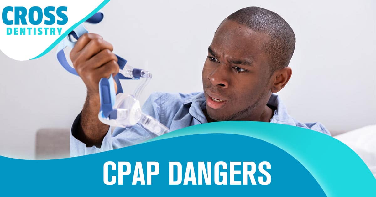 An image of a man in a blue shirt in front of a white background as he clutches the mask of his CPAP and stares at it with a look of betrayal.
